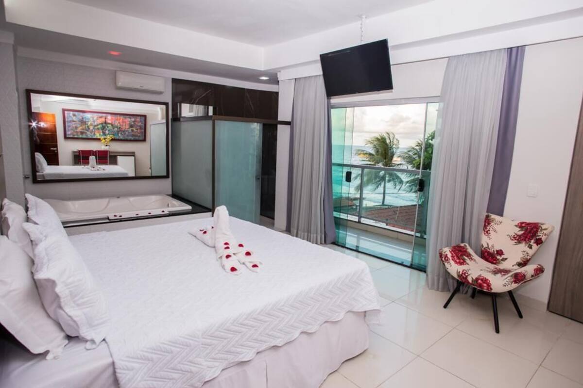 A hotel room with a large bed, a bathroom with a glass shower, a balcony with a view, and a TV mounted on the wall.