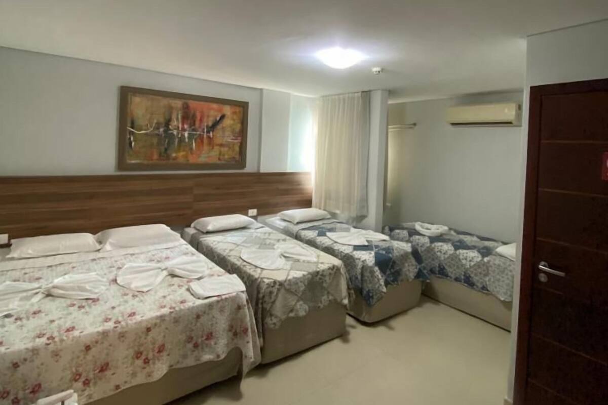 A hotel room with three beds, a wooden headboard, a painting on the wall, and an air conditioning unit.