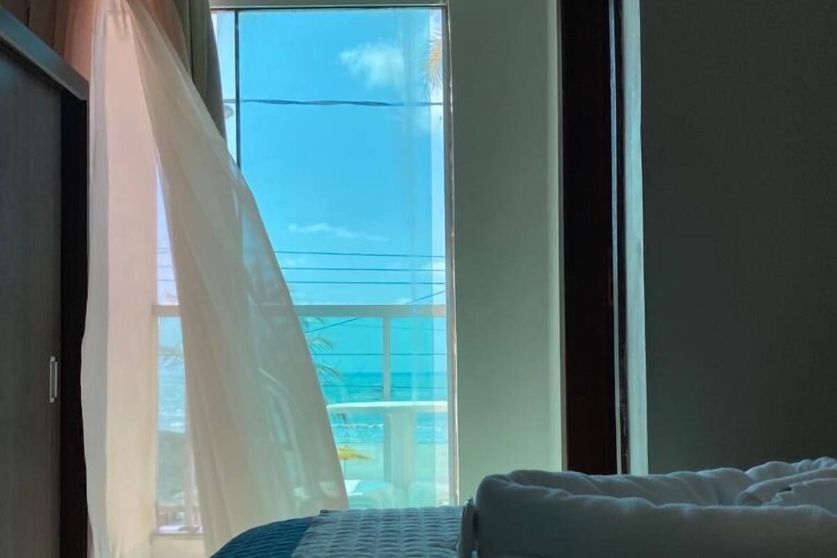 A hotel room with a bed, a window with a view of the sea, and a balcony.