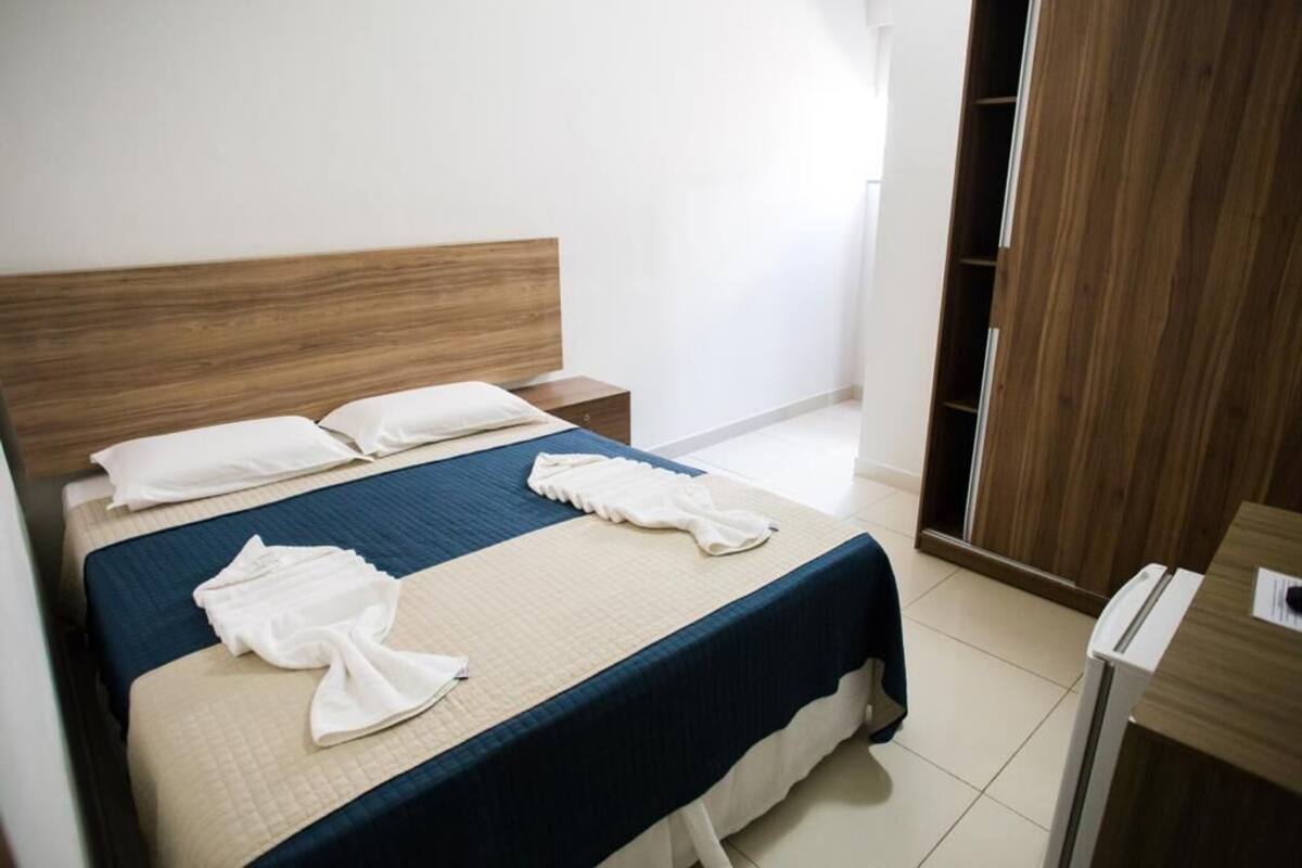 A hotel room with a bed, wooden headboard, bedside tables, and a wardrobe.