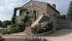 A stone building with a staircase, green shutters, and a gravel driveway. - Stone house, private pool, panoramic view, close to the Gorges de l'Ardèche (Orgnac-l'Aven)