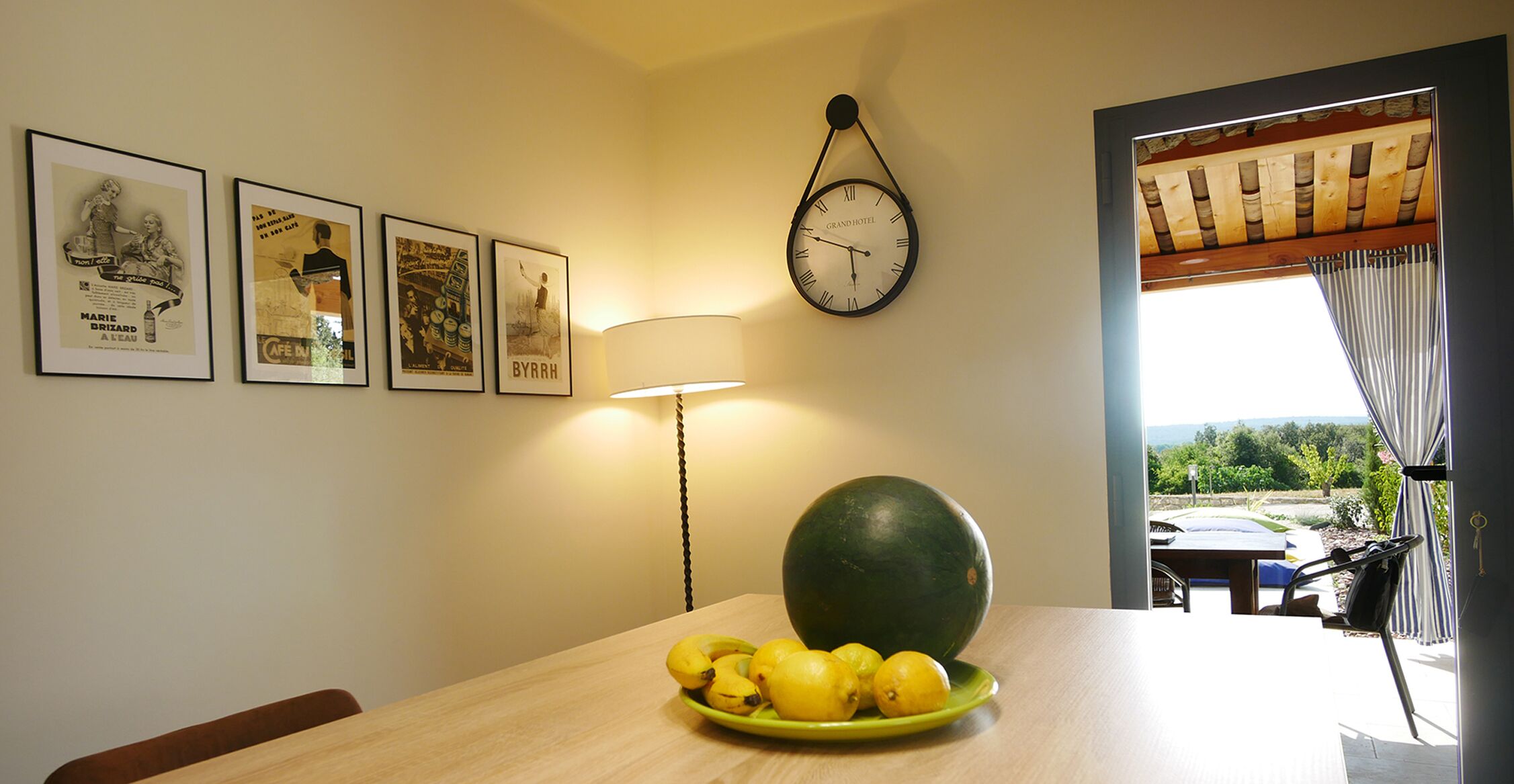 A dining area with a table, a clock, and framed pictures on the wall.