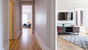 Un corridoio con pavimento in legno che conduce a un soggiorno con televisore, divano e tappeto decorato.