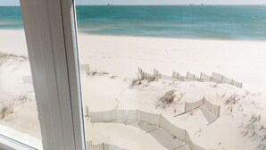 A beach view through a window with a sandy beach and a wooden fence. - Fort Sun, West. Gorgeous 7BR Beachfront. Extra fridges. Private Pool! Sleeps 24. (Gulf Shores)