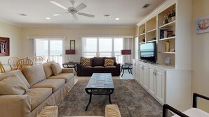 A living room with a beige sofa, a brown sofa, a coffee table, a TV on a cabinet, and a ceiling fan. - Fort Sun, West. Gorgeous 7BR Beachfront. Extra fridges. Private Pool! Sleeps 24. (Gulf Shores)
