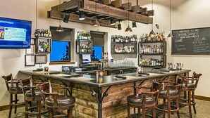 Un espace bar avec des tabourets en bois, un comptoir doté d’une caisse enregistreuse et des étagères remplies de bouteilles.