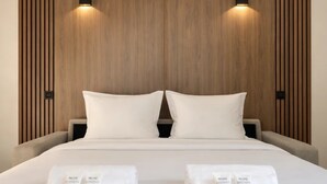 Ett hotellrum med en sänggavel i trä, två sänglampor, en stor säng med vita sängkläder och två handdukar med Nuxes logotyp.