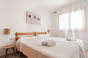 Habitación de hotel con dos camas, un cuadro, una ventana con cortinas translúcidas y una mesita.