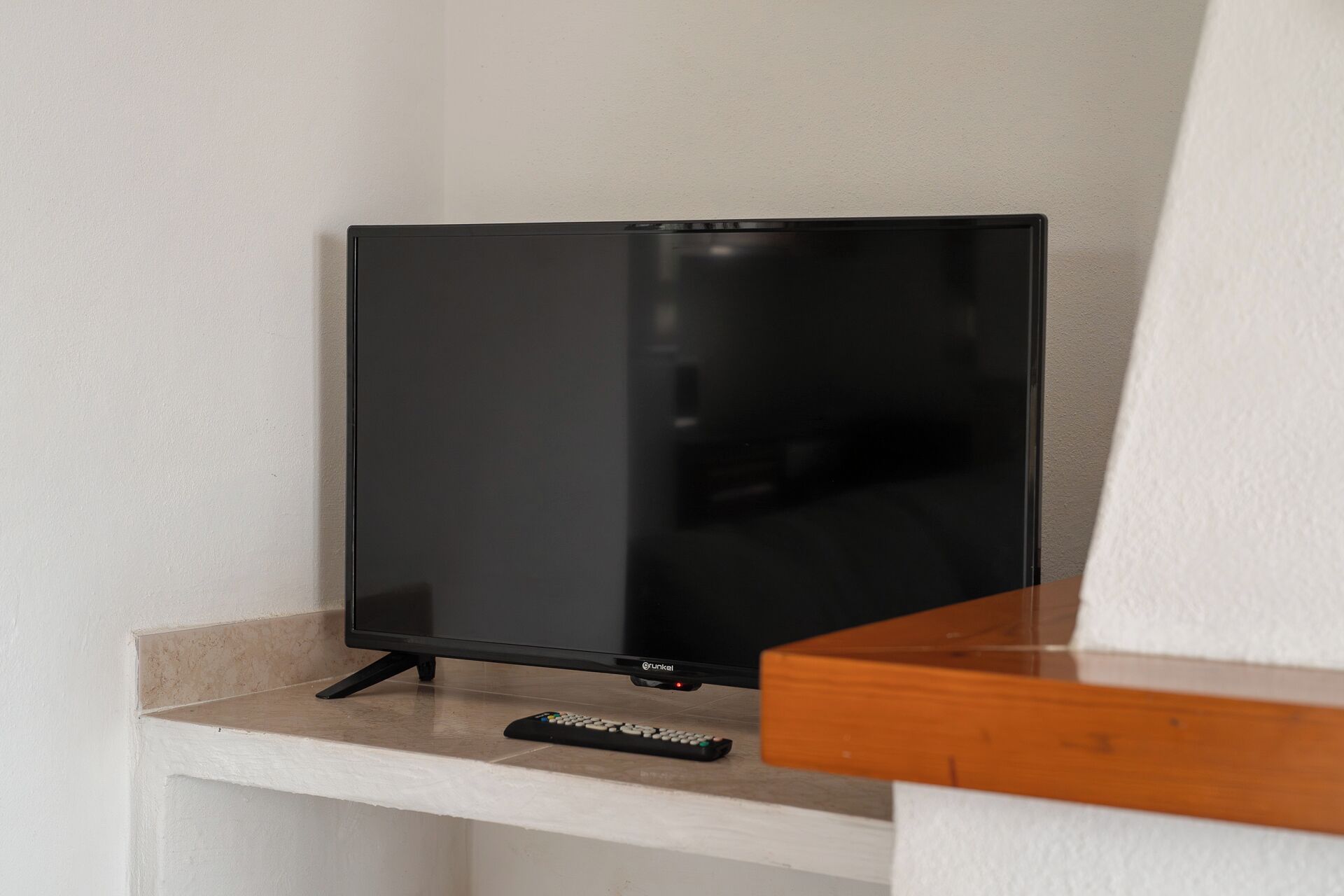 A television on a white stand with a remote control beside it.