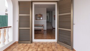 Un pasillo con un banco de madera, suelo de baldosas y una puerta con contraventanas.