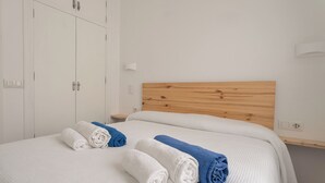 Habitación de hotel con cabecera de madera, cama con ropa blanca, dos toallas enrolladas, una mesita de noche y un armario.