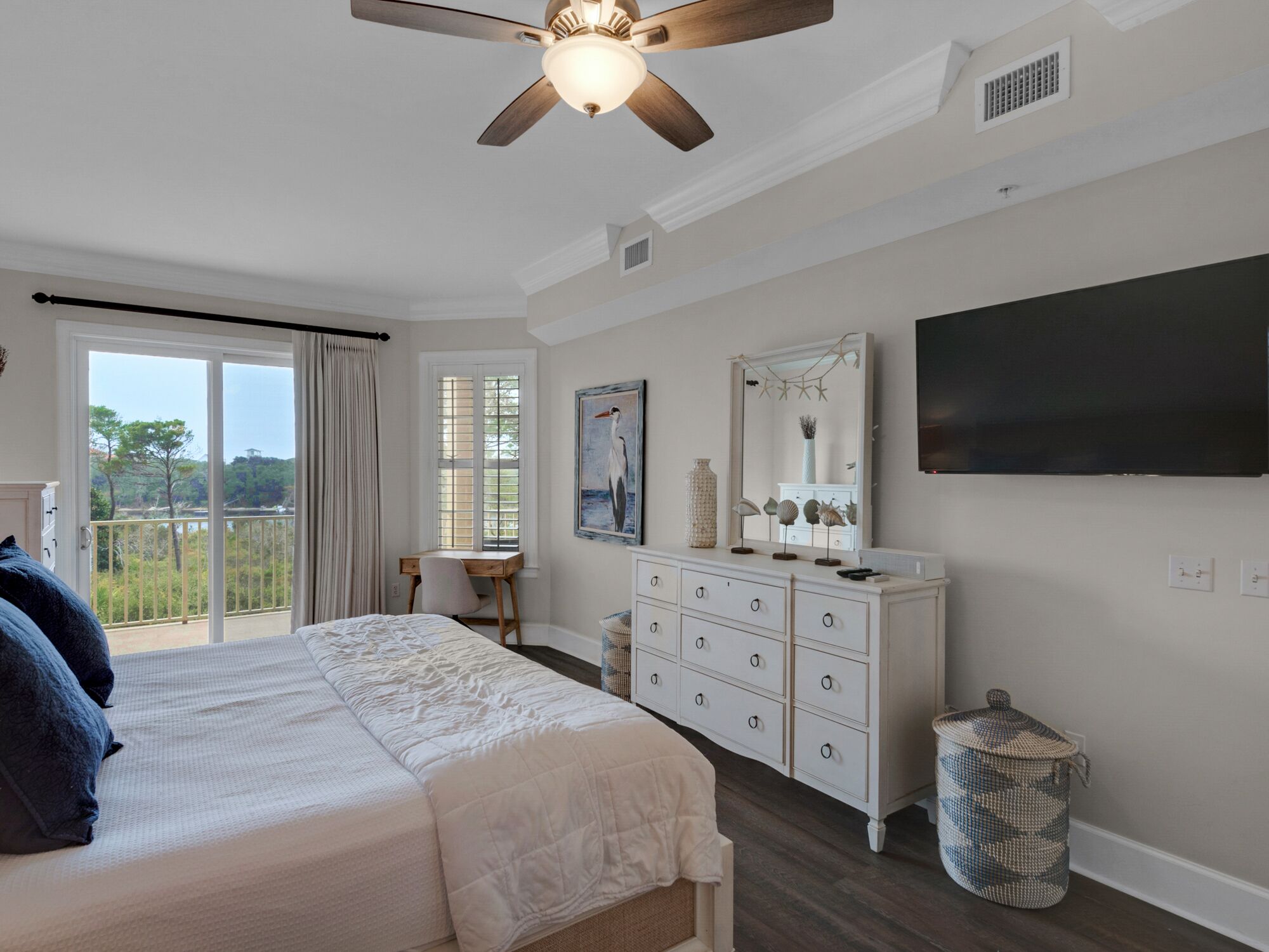 Un dormitorio con cama, cómoda, televisor y vistas al exterior.