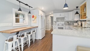 A modern kitchen with white cabinets, a wooden countertop, and bar stools. - The Funky Fuji @Backyard Apple Cottages (Flat Rock)