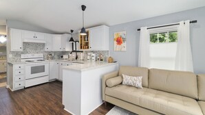 A modern kitchen with white cabinetry, a central island, and a beige sofa. - The Funky Fuji @Backyard Apple Cottages (Flat Rock)