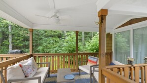 A covered outdoor seating area with a ceiling fan, wooden deck, and a view of a forested area. - The Funky Fuji @Backyard Apple Cottages (Flat Rock)