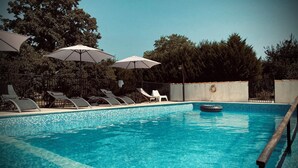 Una piscina con agua azul cristalina, rodeada de sillones de descanso y sombrillas, con árboles al fondo.