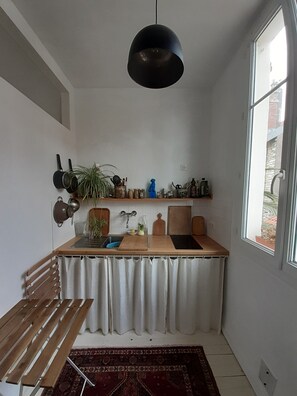 A compact kitchen with a wooden countertop, hanging pots, a potted plant, and a window with a view of the outside.