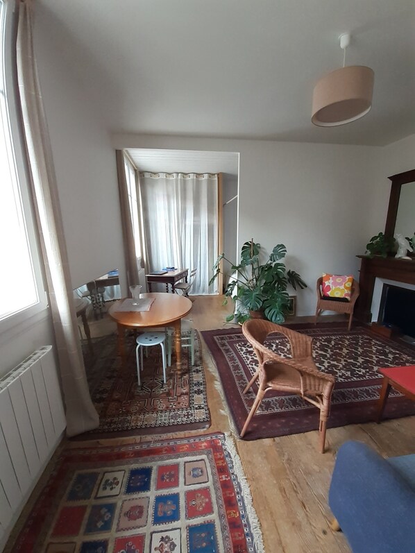 A living room with a round wooden table, two chairs, a patterned rug, a large plant, and a television.