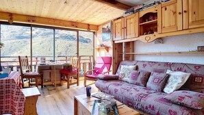 Una cabaña acogedora con interior de madera, un sofá, sillas, una mesa de comedor y vistas a las montañas.