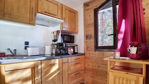 Cocina compacta con armarios de madera, microondas, cafetera y ventana con vista a árboles.