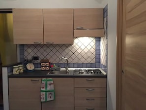 A compact kitchen with wooden cabinets, a gas stove, a sink, and a tiled backsplash.