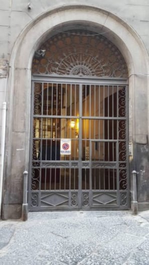 A large, ornate metal gate with intricate designs, leading to a building with a stone facade and an arched entrance.
