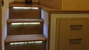 A bedroom with a bed, a nightstand, a dresser, and a staircase with illuminated steps. - CASA CONCETTA (Napoli)