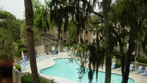 A swimming pool surrounded by lounge chairs and a building with a covered deck. - 2BR Resort condo with free rounds of Golf & Tennis , beach access pool view (Hilton Head Island)