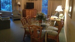 A living room with a glass-top dining table surrounded by wicker chairs, a television, and a sofa. - 2BR Resort condo with free rounds of Golf & Tennis , beach access pool view (Hilton Head Island)