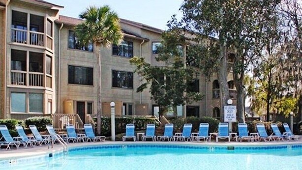 A pool area with lounge chairs and a building with multiple balconies in the background. - 2BR Resort condo with free rounds of Golf & Tennis , beach access pool view (Hilton Head Island)