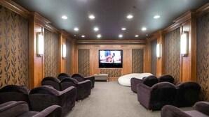 Una sala de cine en casa con televisor de pantalla plana, varios asientos mullidos, piso alfombrado y paneles de madera.