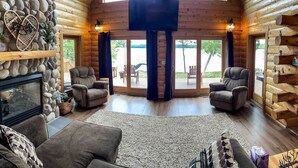 L’intérieur d’une cabane en rondins, avec une cheminée en pierre, deux fauteuils, un canapé et un grand écran de télévision.
