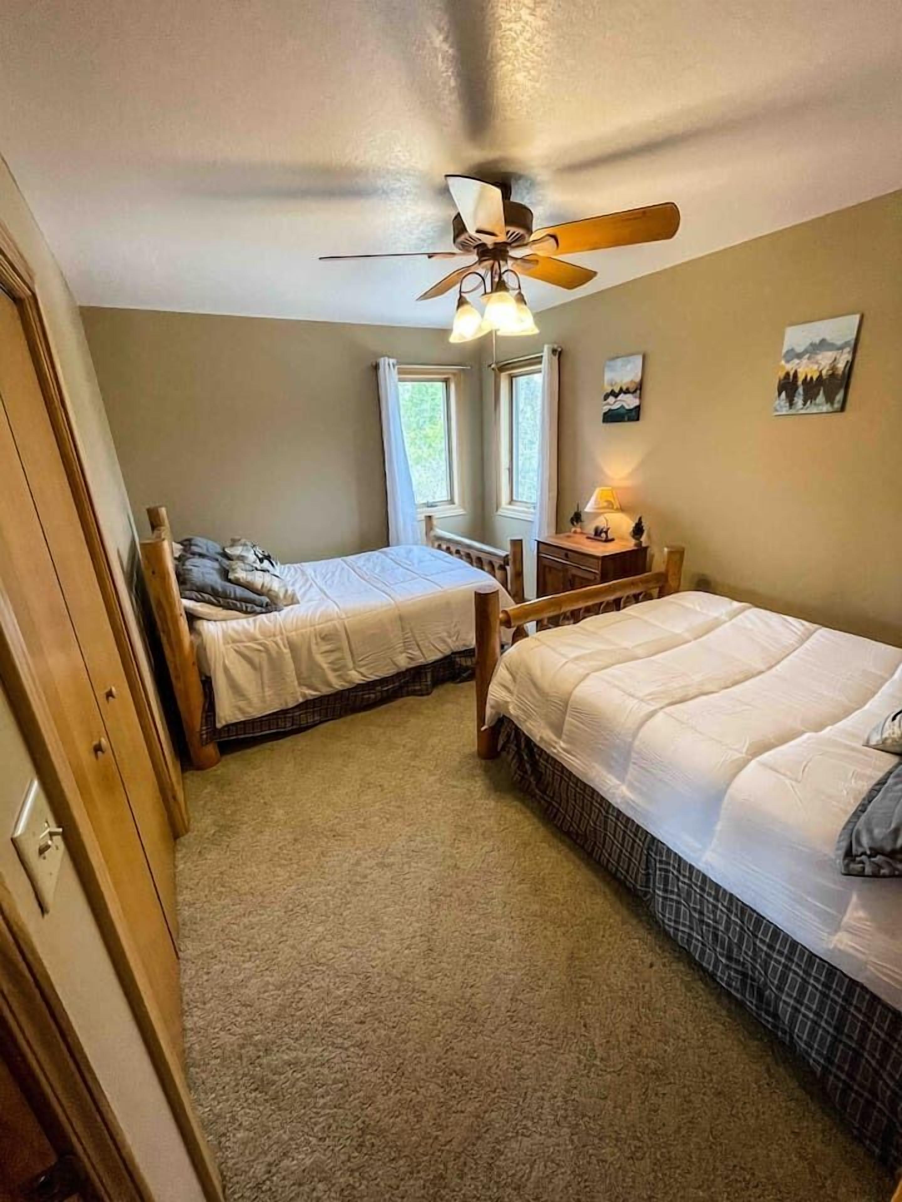 Une chambre avec deux lits, un ventilateur de plafond, une fenêtre avec des rideaux et une table de chevet avec une lampe.