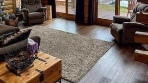 Un intérieur spacieux de chalet en bois, avec un grand téléviseur, des sièges confortables et une vue sur un lac.