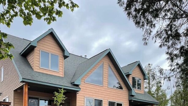 Une maison à deux étages avec un foyer en pierre en premier plan, une terrasse en bois et un espace salon extérieur.