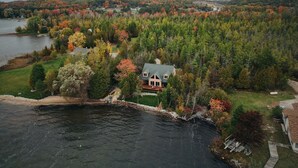 Une maison au bord du lac, entourée d’un feuillage automnal, avec vue sur le lac et les collines lointaines.