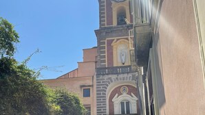 Una calle estrecha con un edificio que tiene una torre del reloj, una planta en maceta y una persona caminando a lo lejos.