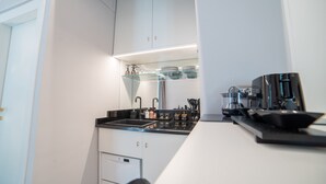 Una cocina compacta con gabinetes blancos, una encimera negra y una cafetera.
