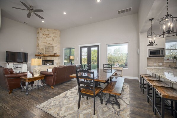 A spacious living room with a fireplace, a dining area, and a kitchen with a large island. - La Casa Rio - Stylish 4/3 Wimberley Blanco Riverfront Acreage, Minutes to Town (Wimberley)
