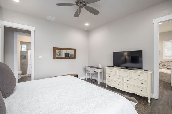 A bedroom with a bed, a TV, a dresser, a desk, and a ceiling fan. - La Casa Rio - Stylish 4/3 Wimberley Blanco Riverfront Acreage, Minutes to Town (Wimberley)