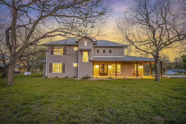 A two-story house with a covered porch and a garage, surrounded by a well-maintained lawn and trees.