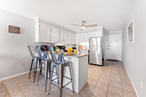 Una cocina moderna con armarios blancos, un refrigerador de acero inoxidable y una zona con taburetes de bar.