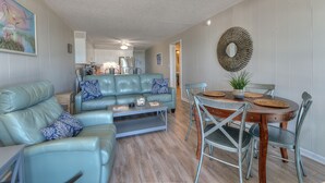 Sala de estar com sofá azul, mesa de centro e área de jantar com mesa de madeira e cadeiras de metal.