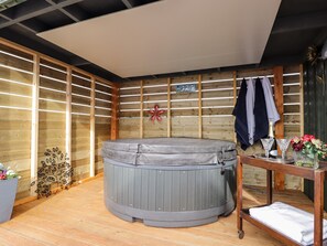 Un jacuzzi en una habitación de madera con suelo de madera, una mesa con bebidas y una toalla sobre un banco.