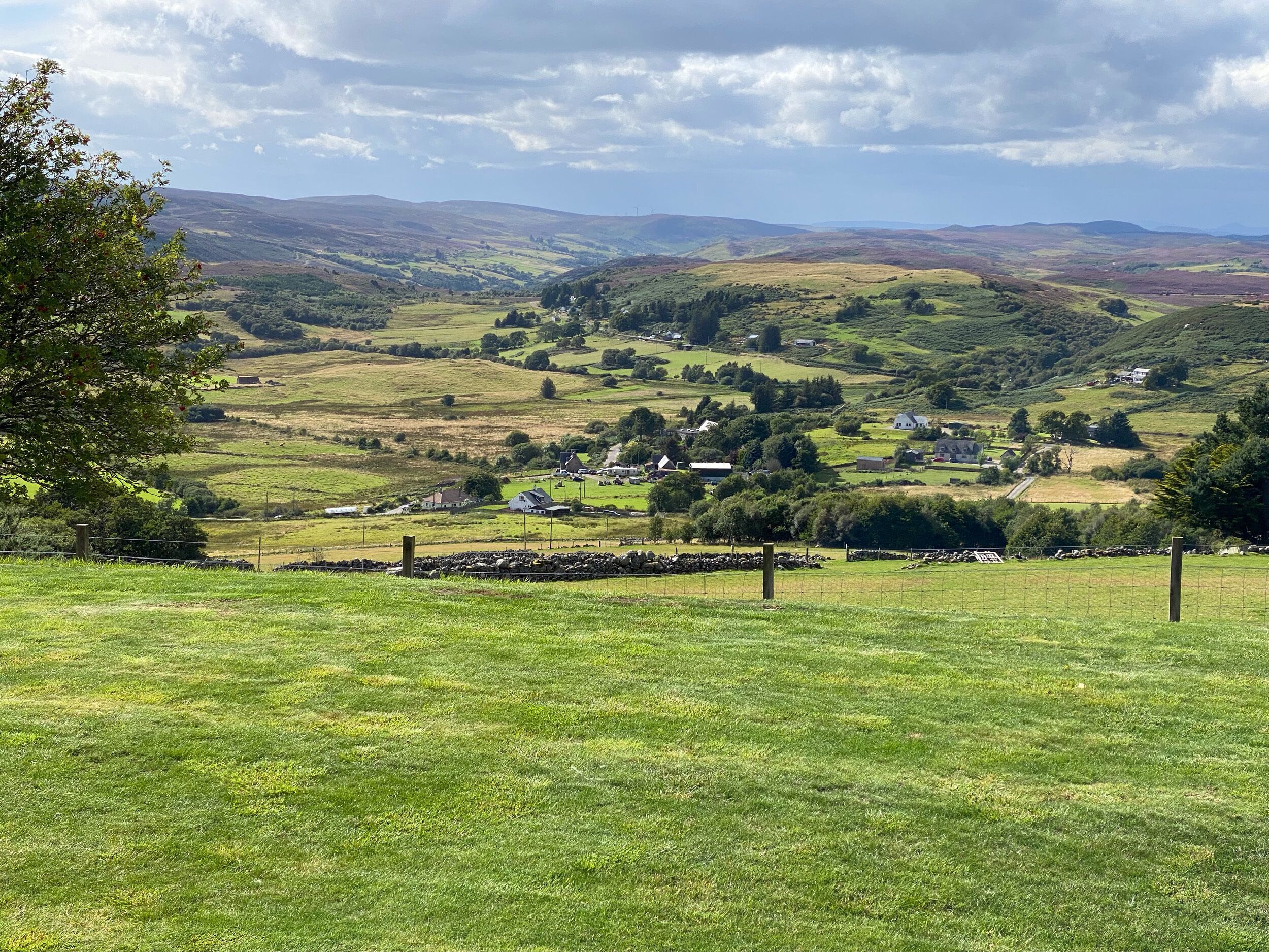 Un paisaje rural con colinas onduladas, casas dispersas y un campo cercado.