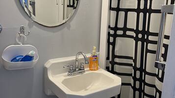 A bathroom with a white sink, a mirror, a bottle of soap, and a black and white patterned shower curtain.
