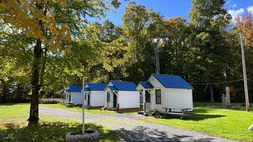 A row of small, single-story cabins with blue roofs, surrounded by trees and a grassy area.