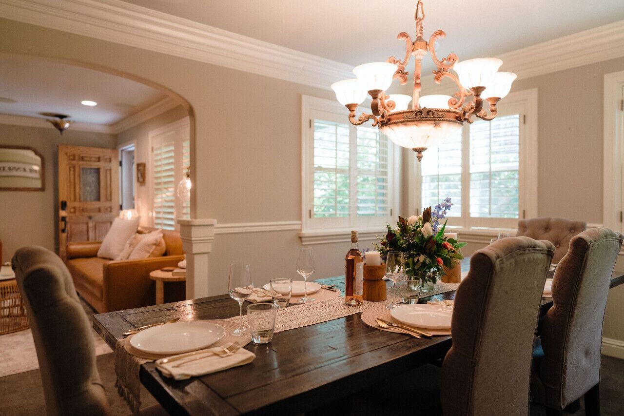 A dining area with a dark wooden table set for four, a chandelier, and a window with blinds.