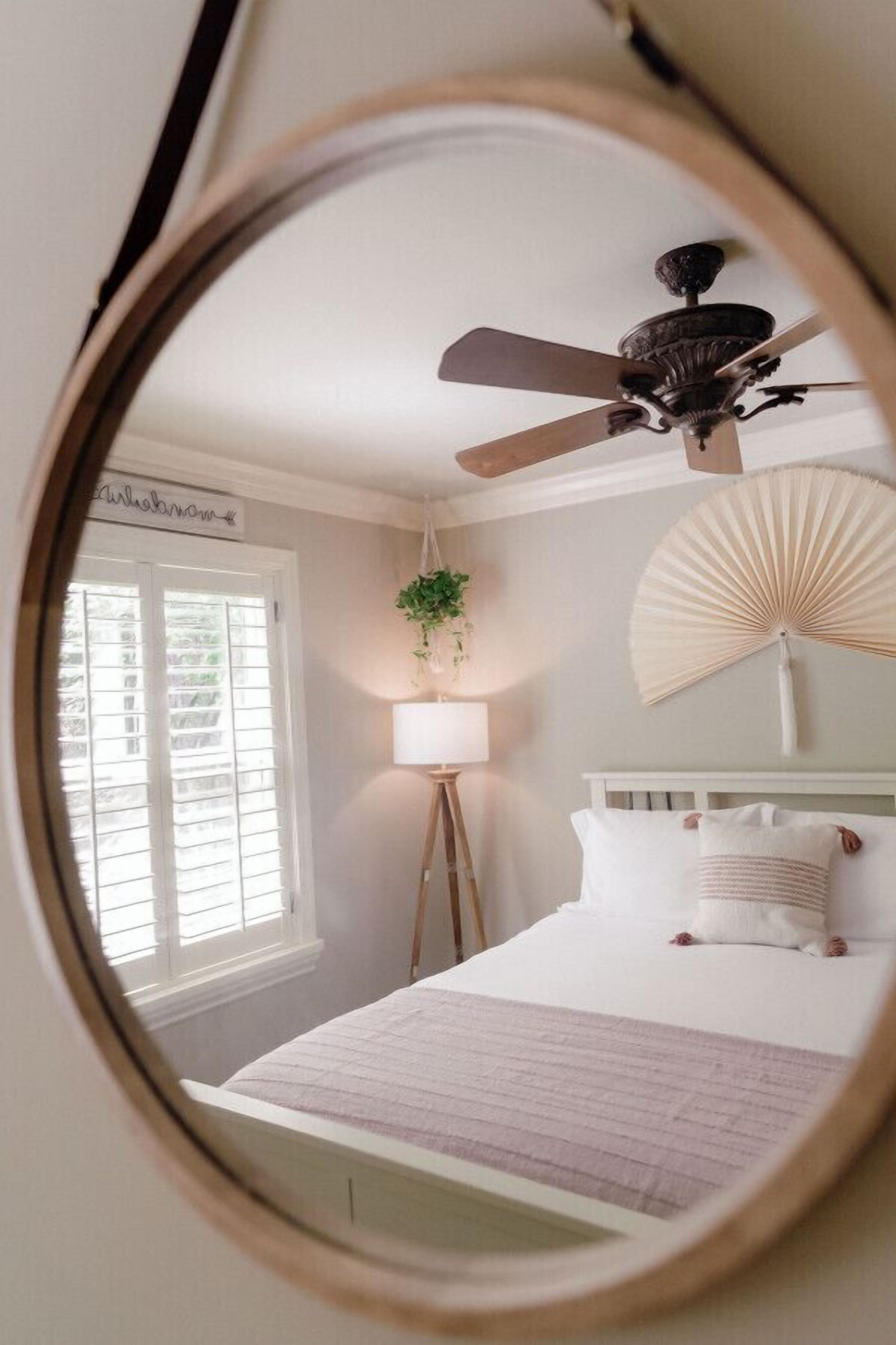 A bedroom with a bed, a ceiling fan, a bedside lamp, a window with blinds, and a wall-mounted fan.