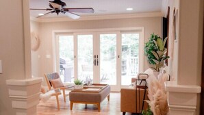 A spacious living room with a wooden floor, a ceiling fan, a sofa, a coffee table, and a large window with a view of the outdoors. - Luxury Home, Hot Tub Walk To Downtown Nevada City (Nevada City)